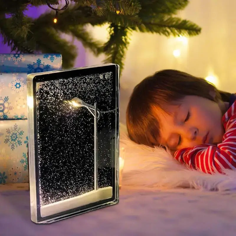 Child sleeping beside a snowy scene nightlight featuring a street lamp, perfect for creating a cozy atmosphere.